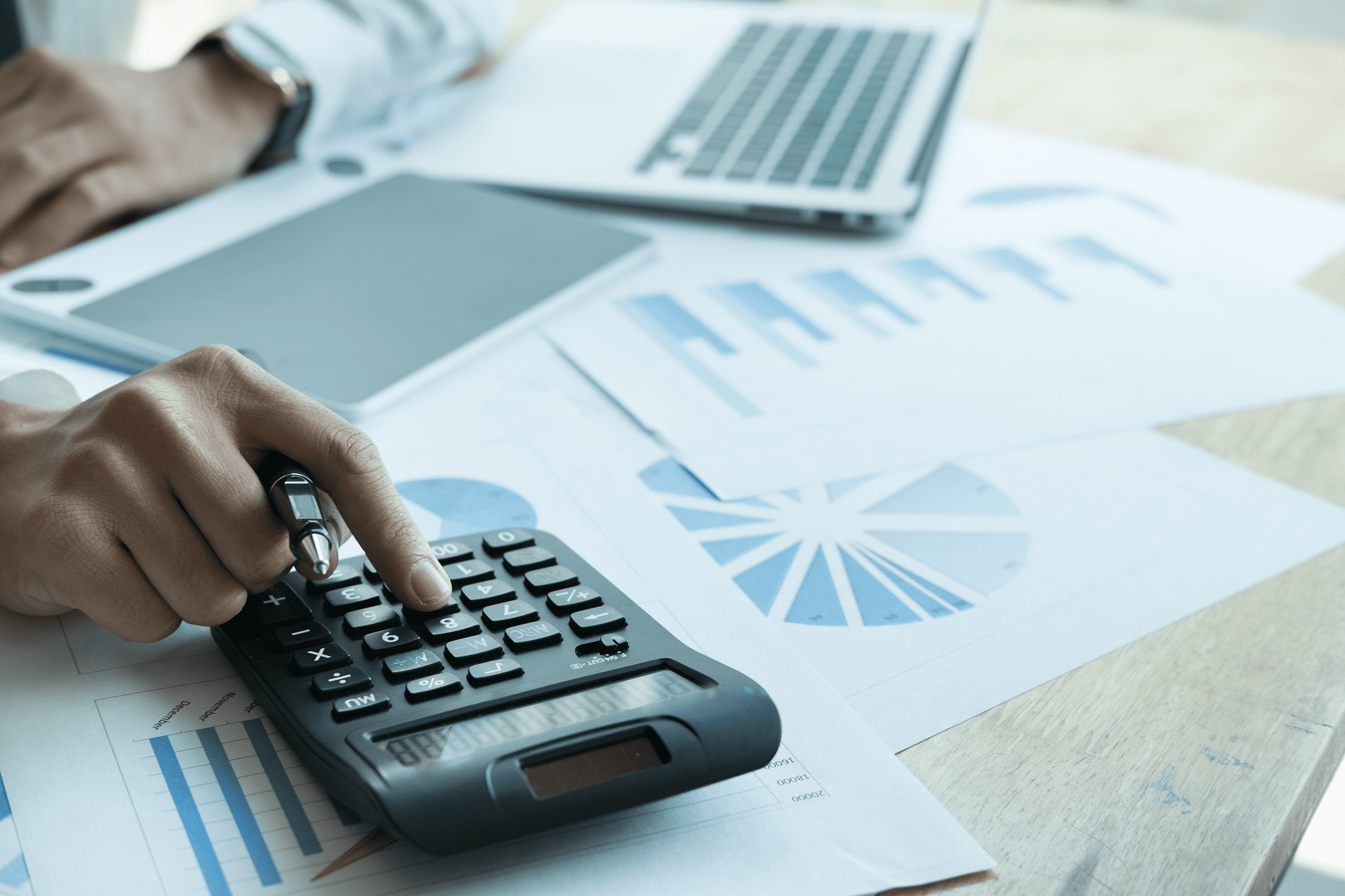 Person using calculator with financial charts.